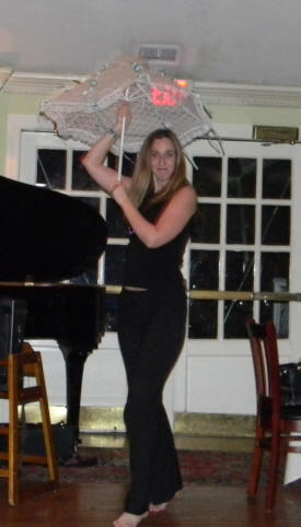 tall, slim blonde in black sleeveless top and slacks dancing in stocking feet with flowered umbrella