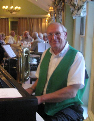 Dick in green vest, on piano, with crowd in background