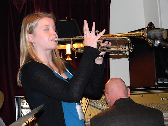 Bria with eyes closed, four fingers pointing straight up, playing muted trumpet