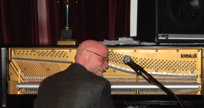 Jeff Barnhart sitting in front of the vertical strings
			of the open front, Kimball piano and laughing