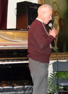 Robin looking at audience and speaking into mike, with picture of naked lady behind him