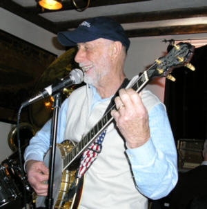 A smiling and singing Joel Schiavone, wearing a cap - brim in front