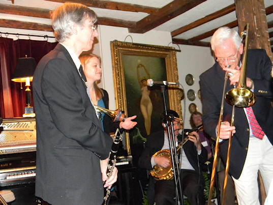 Joe and Bria watch Craig on trombone.
			In the background, there's a portrait of a naked lady, full front view, with arms outstretched way over her head.
			 She appears in almost every photo.