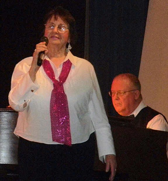 Deanna Kowalczyk holding dead mic, with Wayne at piano